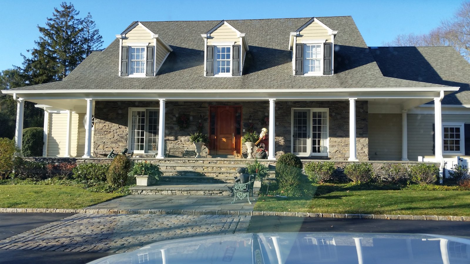 Architectural asphalt shingle roof on a Long Island Cape Cod style home with stone front and wrap-around porch